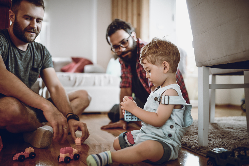 Homosexuelles Paar mit Tochter sitzen in einem Kinderzimmer und spielen miteinander