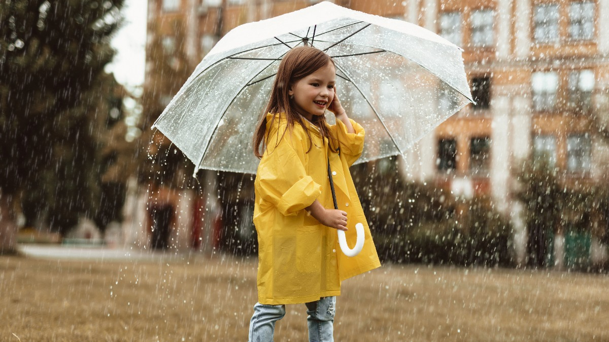 Fröhliches kleines Mädchen steht mit Regenschirm im Regen