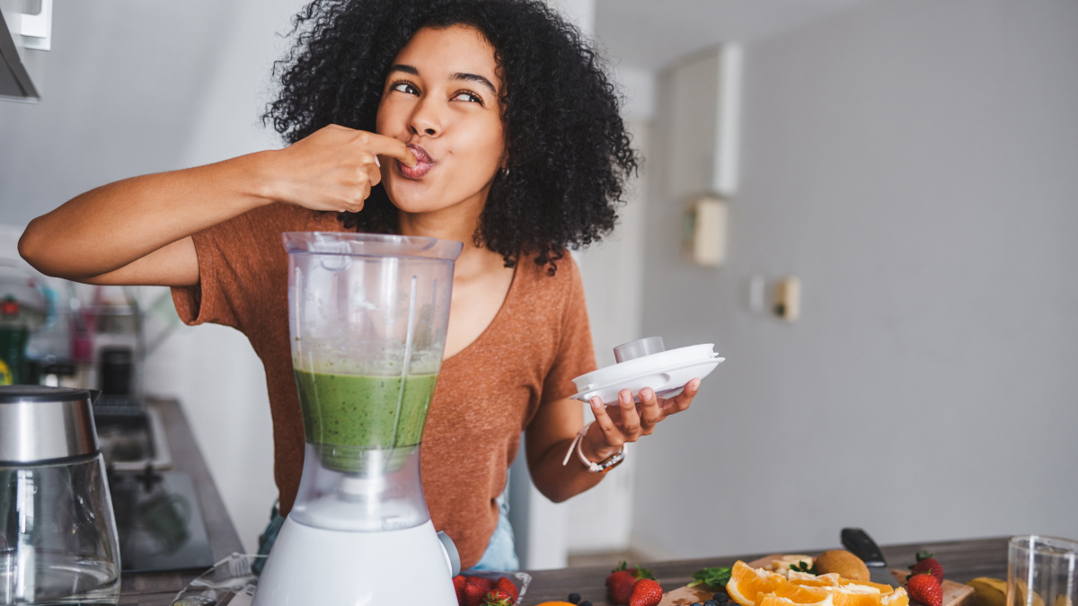 Junge Frau probiert Smoothie aus dem Mixer